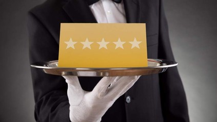 Ein Kellner hält ein Tablet auf dem sich eine goldene Karte mit fünf Sternen befindet