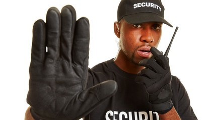 Mann vom Wachschutz spricht in Funkgerät und streckt seinen Arm aus