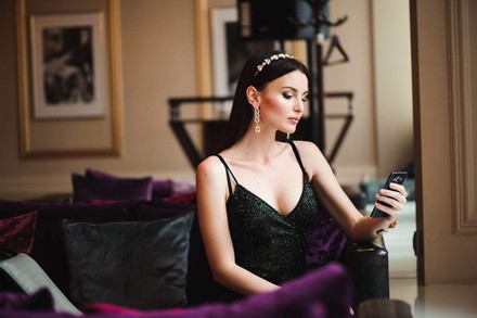 Eine hübsche Frau sitzt auf einem Sofa und blickt auf ihr Smartphone