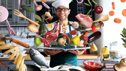 Ein Koch mit einem Kochbuch aus dem alle möglichen Zutaten fliegen