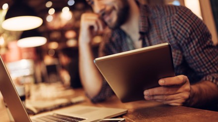 Junger Mann sitzt im Café über Laptop und Tablet gebeugt