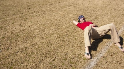 Mann liegt mit Cap in Gesicht auf Gras