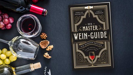 das Standardwerk Master Wein-Guide liegt auf einem Tisch, daneben zwei Weinflaschen und zwei Weingläser