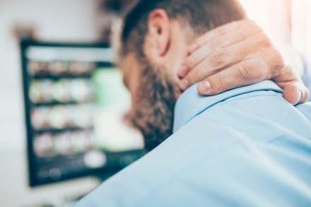 Ein Büroarbeiter sitzt vor seinem Computer und drückt eine Hand gegen seinen Nacken