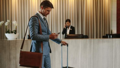 Ein Geschäftsmann blickt in einer Hotelrezeption auf sein Handy