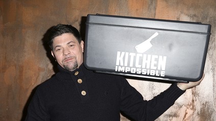 Tim Mälzer mit dem Logo von Kitchen Impossible