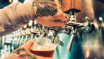 Zwei tattoowierte Hände zapfen ein Bier