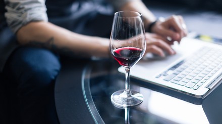 Nahaufnahme eines Mannes, der mit einem Glas Rotwein vor dem Laptop sitzt
