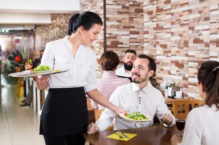 Eine freundliche Servicekraft serviert lächelnden Gästen Salate