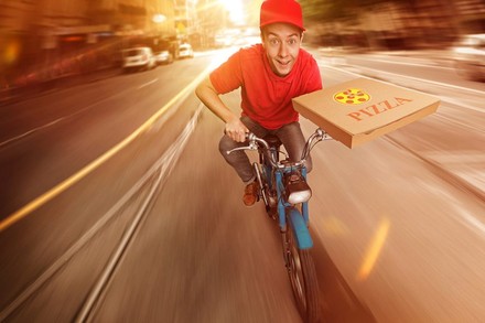Pizzalieferant auf Mofa mit Pizzaschachtel in der Hand