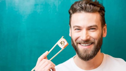 Mann hält Sushi in Essstäbchen