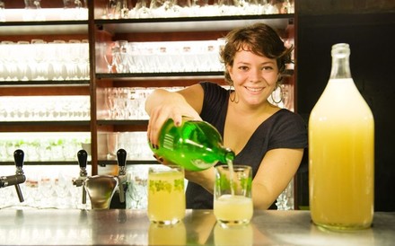 Eine lächelnde Barmitarbeiterin gießt ein Getränk aus einer großen Flasche in ein Glas