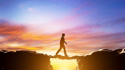 Mann läuft über anderen Mann, welcher mit seinem Körper eine Brücke zwischen zwei Felsen spannt