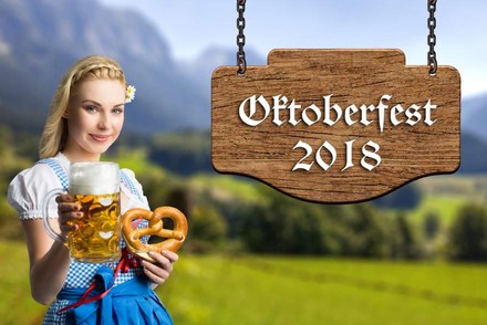 Eine Frau im Dirndl preist Bier und Brezen vor einem Schild mit der Aufschrift Oktoberfest 2018 an