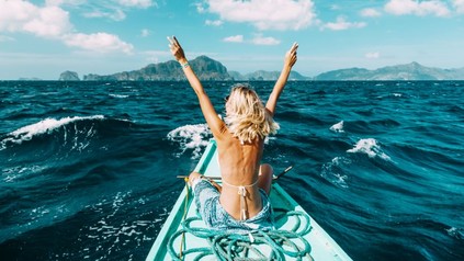 Blonde Frau auf Boot streckt Arme in die Luft