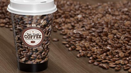 Ein Kaffeebecher mit der Aufschrift Fair Trade Coffee vor einem Menge Kaffeebohnen