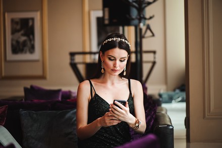 Eine hübsche Frau sitzt auf einem Sofa und blickt auf ihr Smartphone