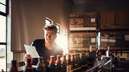 Brauer steht mit Zettel in der Hand vor der Abfüllanlage