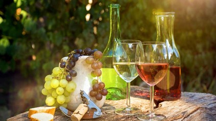 Weinflaschen, Weingläser und Trauben auf einem Tisch im Freien