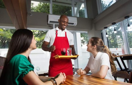 Ein Mann schwarzer Hautfarbe bedient fröhlich zwei Gäste im Restaurant
