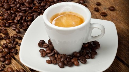 Eine Tasse gefüllt mit Espresso und Kaffeebohnen drumherum