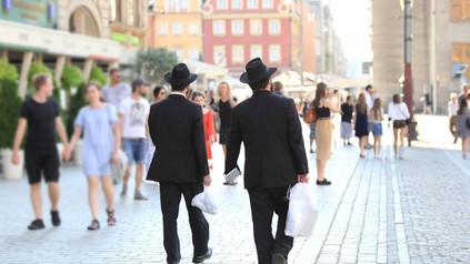 Zwei schwarz gekleidete Männder mit Hüten gehen eine Straße entlang