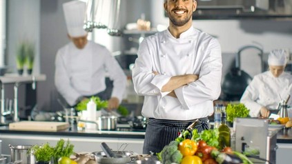 Ein grinsender Koch mit Gemüse in der Küche