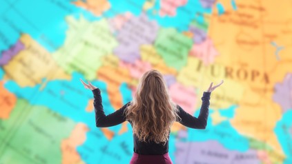 Frau steht mit gehobenen Armen vor einer Weltkarte