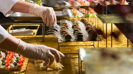 Ein Gastronomiemitarbeiter in Plastikhandschuhen richtet ein Buffet her