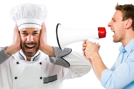 Ein Mann im Hemd schreit einen Koch mit einem Megafon an