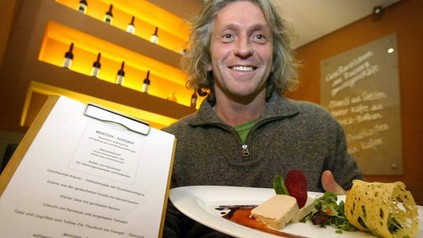 Bernhard Reiser lächelnd mit einer Urkunde und einem Teller mit Essen in der Hand