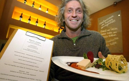 Bernhard Reiser lächelnd mit einer Urkunde und einem Teller mit Essen in der Hand