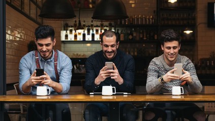 Drei Männer sehen in ihr Smartphone in Café