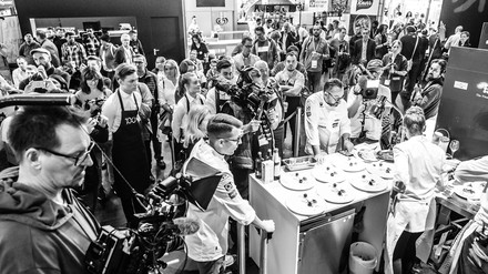 Eine Köchin bereitet sieben Tellergerichte zu und wird dabei von einer Jury, Kamerateams und Zuschauern beobachtet