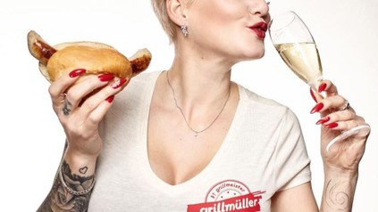 Frau trinkt Sekt und hat Bratwurstsemmel in der Hand