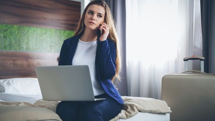 Geschäftsfrau auf Bett mit Laptop und Smartphone