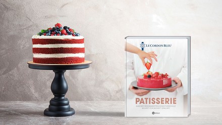 Das Buch „Patisserie“ von Le Cordon Bleu steht neben einer Torte mit Waldbeeren