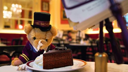 Bär in Pagengewand vor Kuchen auf Tisch