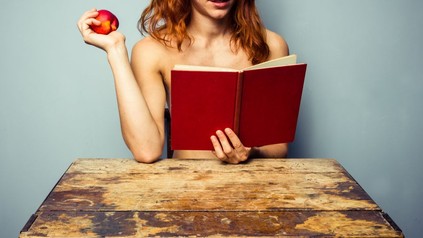 Nackte Frau liest ein Buch und hält einen Apfel