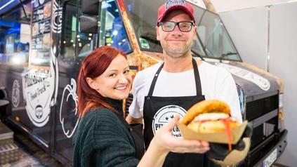 Zwei Menschen auf einer Messe, die vor einem Foodtruck etwas essen