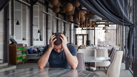 Verzweifelter Gastronom sitzt an einem Tisch in seinem leeren Restaurant/Café