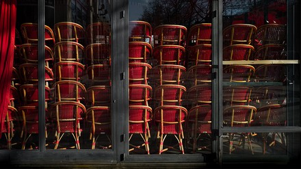 Blick von außen durch verglaste Fensterfronten in ein geschlossenes Restaurant, in dem rote Stühle gestapelt sind