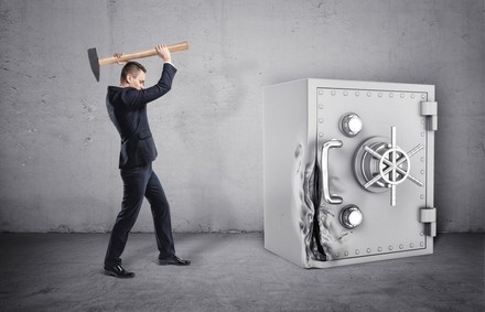 Mann in Anzug hämmert mit Hammer auf Tresor ein