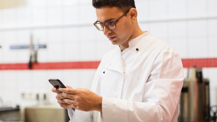 Chefkoch mit Smartphone im Restaurant