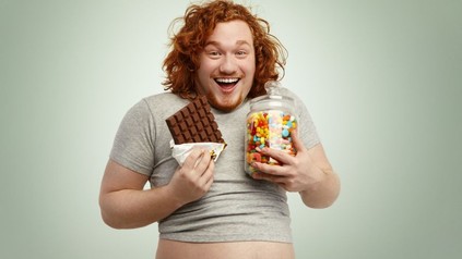 Dicker Mann mit roten Haaren hält Schokoladentafel und ein Glas mit Süßigkeiten in den Händen