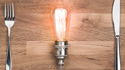 Ein Messer, eine Gabel und eine leuchtende Glühbirne auf einem Tisch