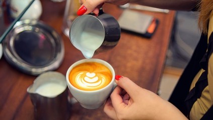 Frau schüttet Milchschaum in Kaffee