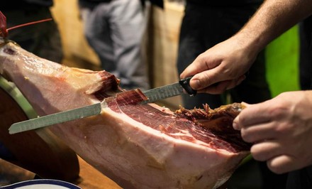 Ein Iberico-Schinken, von dem gerade eine hauchdünne Scheibe abgeschnitten wird