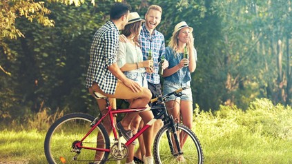 Freundesgruppe mit einem Fahrrad in der Natur trinkt Bier aus Flaschen.