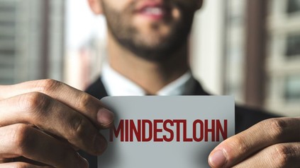Mann hält Zettel mit Inschrift "Mindestlohn" in den Händen